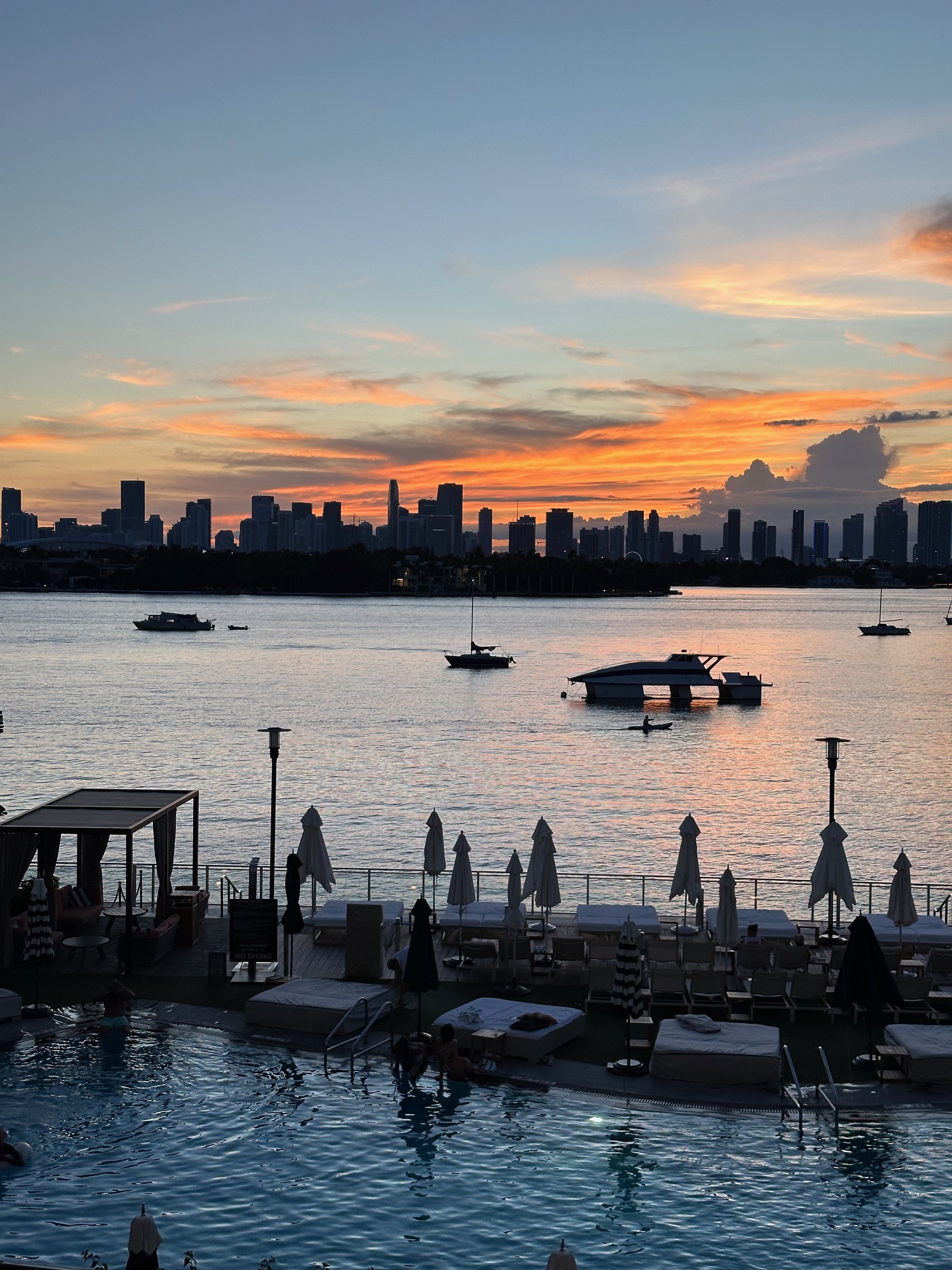 Pool deck at sunset with bay, skyline, and lounge chairs