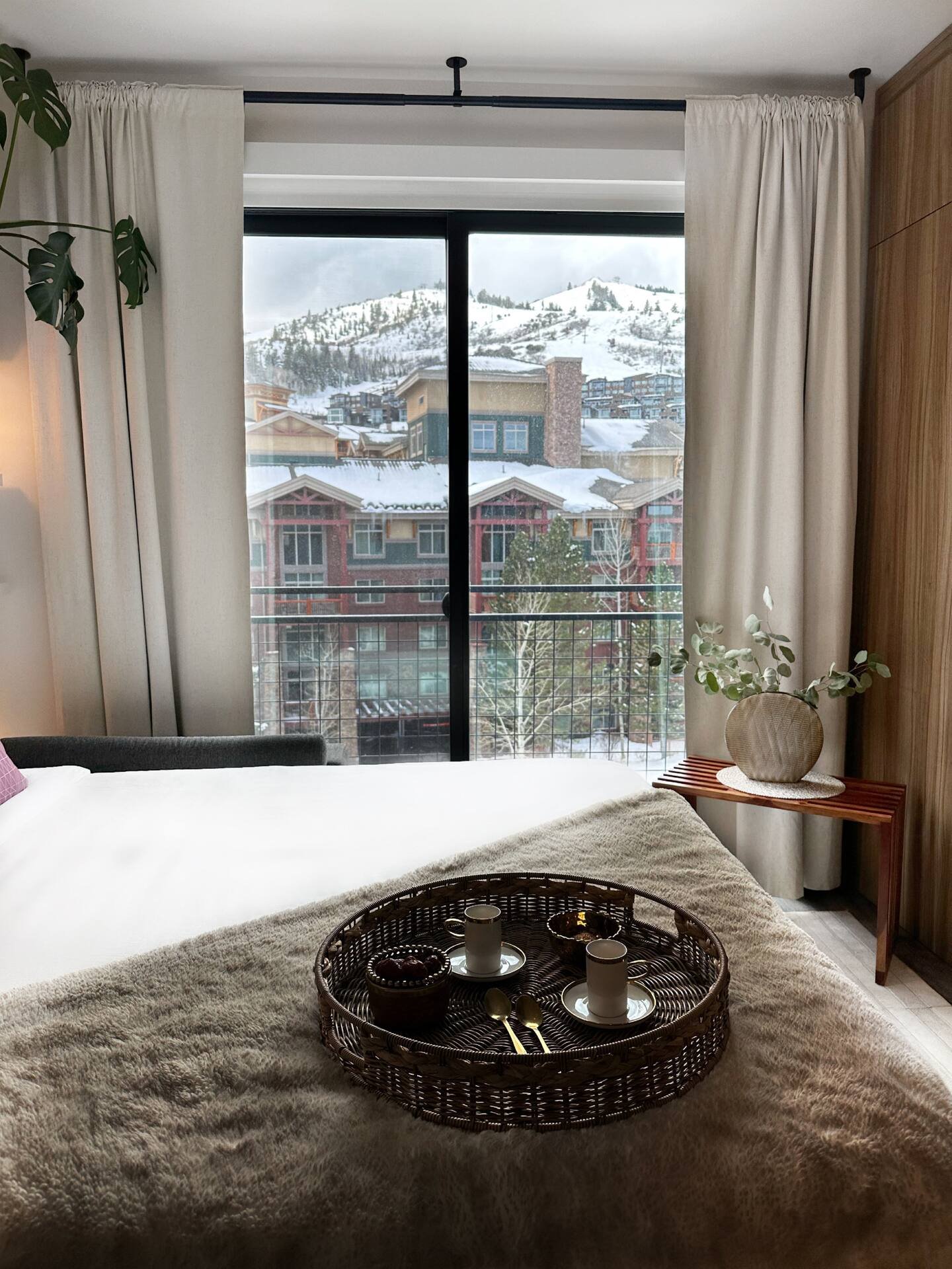 Cozy queen bed with wicker tray and mountain slope view through large window