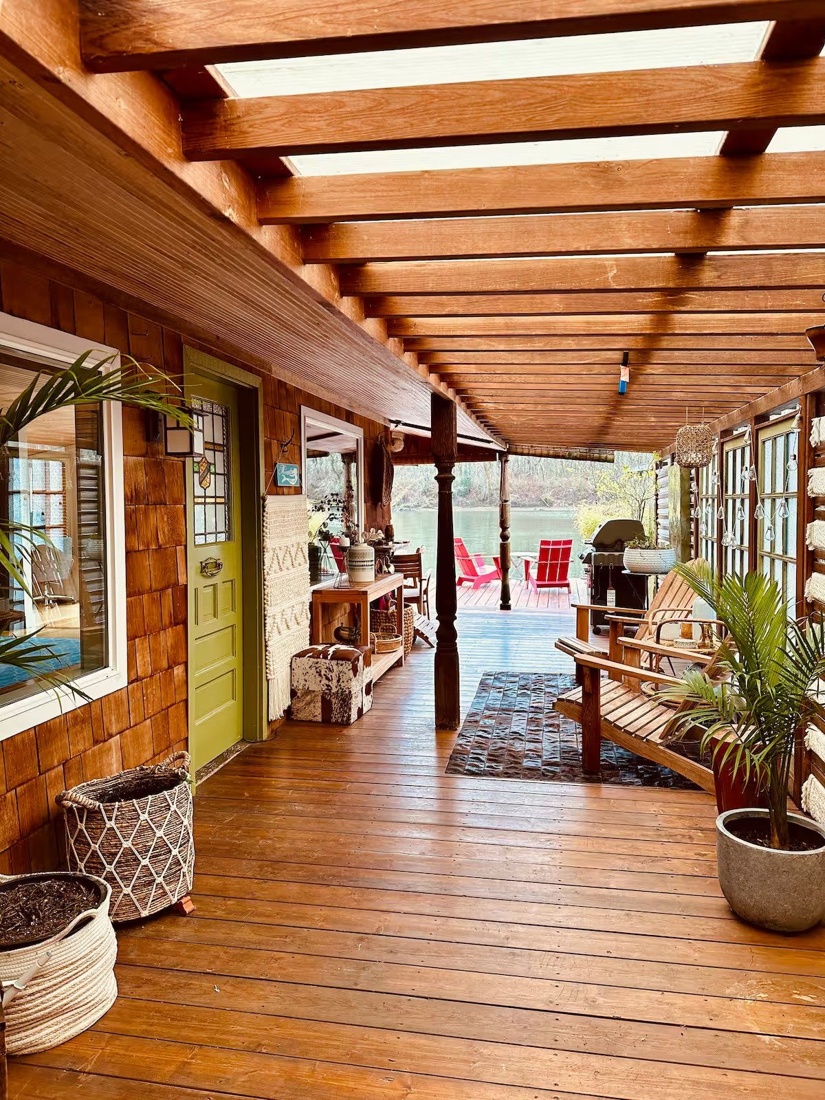Covered cedar porch with Adirondack chairs, plants, and wood beams overlooking the river