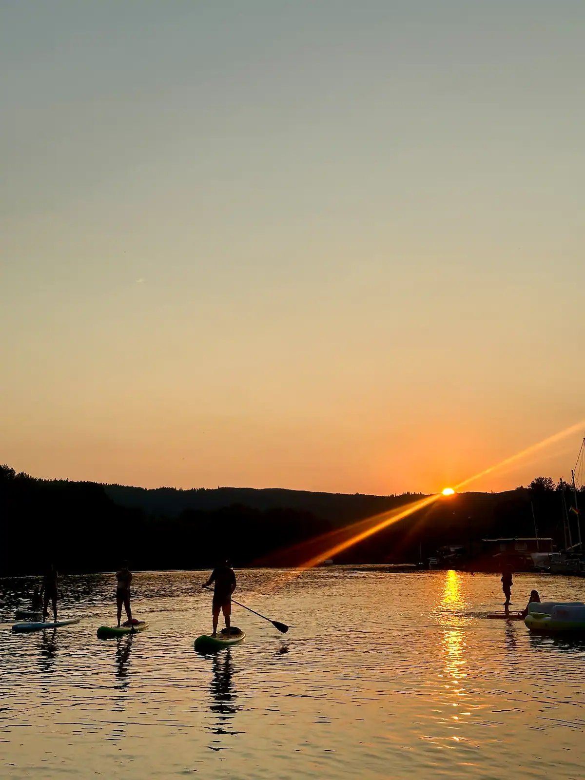 Paddleboarders silhouetted against golden sunset on the river